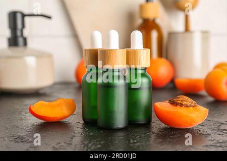 Bottiglie con olio cosmetico e albicocche sul tavolo nero Foto Stock