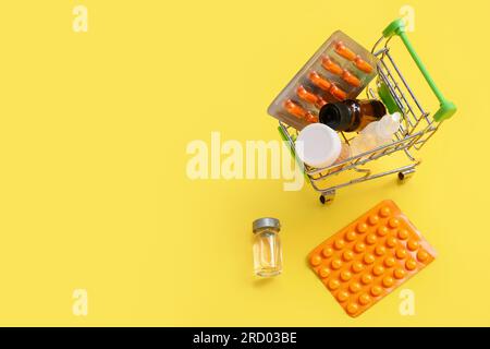 Mini carrello con diversi farmaci su sfondo giallo Foto Stock