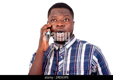 un giovane con una camicia a maniche corte in piedi su uno sfondo bianco che parla al cellulare con un look sorpreso. Foto Stock