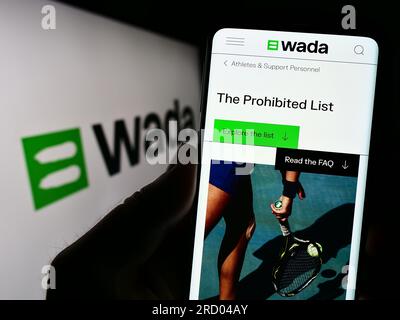 Persona che tiene uno smartphone con pagina web dell'organizzazione World Anti-doping Agency (WADA) sullo schermo con logo. Concentrarsi sul centro del display del telefono. Foto Stock