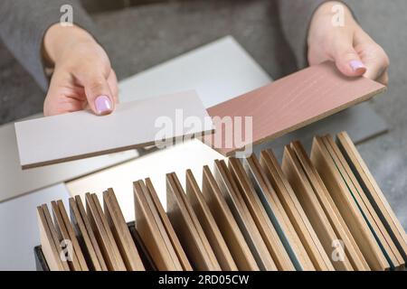 Campioni di legno di specie diverse nelle mani. Una donna sceglie un campione di legno di colori diversi per la produzione di mobili o interni Foto Stock