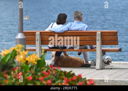 Rottach Egern, Deutschland. 17 luglio 2023. Una coppia anziana con un cane siede su una panchina a Rottach Egern sulle rive del lago Tegernsee il 07/17/2023 l'uomo mette il braccio intorno alla moglie? Credito: dpa/Alamy Live News Foto Stock