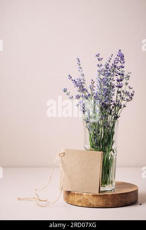 Bouquet di lavanda in un bicchiere e carta bianca mockup su sfondo beige. Foto Stock