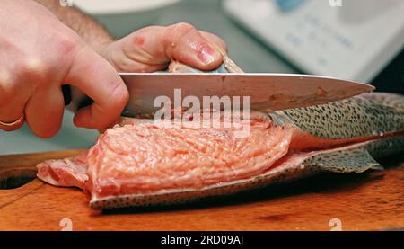 il marito rimuove la pelle dai pesci rossi su una tavola di legno con un coltello, prepara sushi, orizzontale, sfondo, sfocato Foto Stock