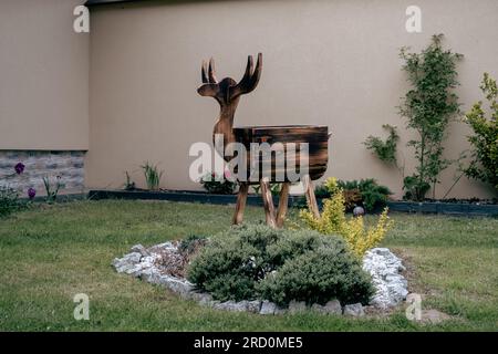 Scultura in legno da giardino di un cervo - sullo sfondo di fiori e un muro. Decorazione a legna. Foto Stock