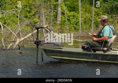 Un uomo maturo pesca in un lago dell'Arkansas meridionale. E' entrato nella sua barca di pesce e ha pescato nelle acque alla ricerca di pesci. Ha sulla tuta e un cappello. Foto Stock