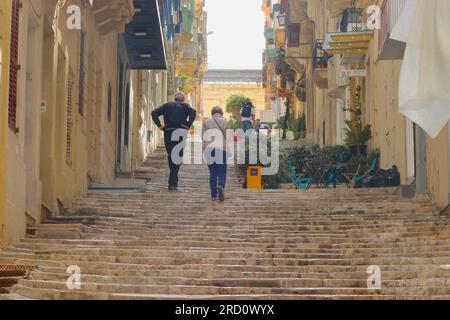 I turisti salgono a malapena la lunga serie di scalini a St. Ursula Street, la Valletta, Malta, aprile 2023. Foto Stock