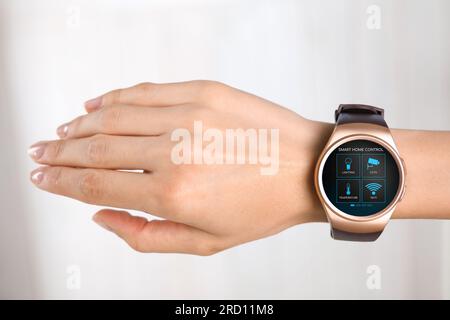 Donna che indossa uno smartwatch con le icone dell'app Smart Home Control in esposizione su sfondo chiaro, primo piano Foto Stock