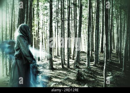 Una donna con un abito con cappuccio balla in una foresta magica. La foto evoca una qualità fantasma ultraterrena. Foto Stock