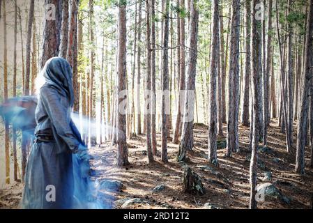 Una donna con un abito con cappuccio balla in una foresta magica. La foto evoca una qualità fantasma ultraterrena. Foto Stock