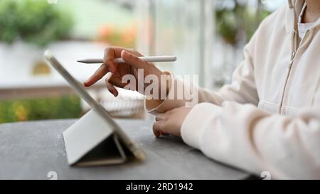 Immagine ravvicinata di una freelance asiatica che usa il suo tablet digitale mentre si trova in una caffetteria durante il fine settimana. nomade digitale, telelavoro Foto Stock