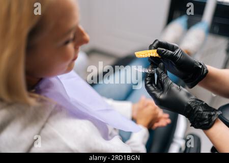 Vista ravvicinata e ad alto angolo di un ortodontista non riconoscibile nei guanti che mostra gli allineatori a una giovane paziente durante la consultazione presso la clinica odontoiatrica. Foto Stock