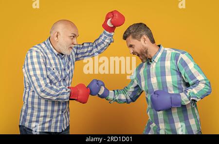 uomini arrabbiati di due generazioni che combattono isolati sul giallo. uomini di generazione che combattono in studio. Foto Stock