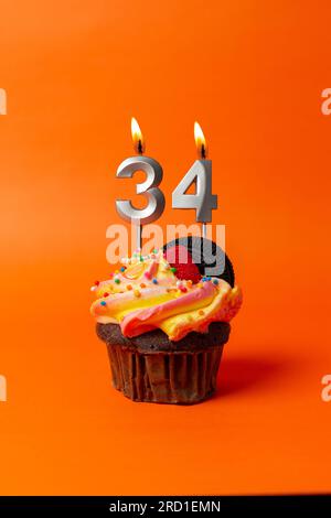 torta di compleanno con numero 34 - cupcake su sfondo arancione con candele di compleanno Foto Stock