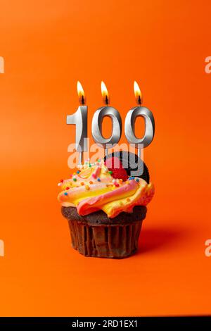 torta di compleanno con numero 100 - cupcake su sfondo arancione con candele di compleanno Foto Stock