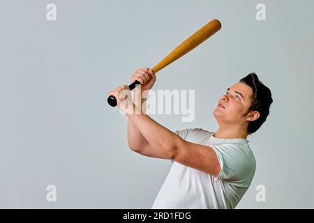 Un uomo con un pipistrello in mano oscilla su uno sfondo grigio Foto Stock