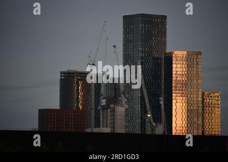 Manchester, Regno Unito. 18 luglio 2023. Luce dell'alba mentre il sole nascente inizia ad illuminare i blocchi della torre di Deansgate Square con gru a torre di fronte. Il Manchester City Council ha concordato piani per costruire più di 1.500 appartamenti in tutto il centro di Manchester, tra cui due nuovi grattacieli. Quasi 1.000 appartamenti saranno costruiti in due edifici a 51 piani in Great Jackson Street, accanto agli importanti edifici a torre di Deansgate Square. I critici hanno sostenuto che pochi di questi appartamenti saranno accessibili e più residenti eserciteranno pressioni sui servizi esistenti, come il servizio sanitario nazionale e le scuole. Credito: Terry Waller/Alamy Live News Foto Stock