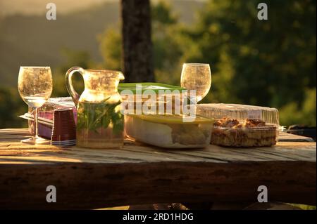 Cibo e bevande su un tavolo di legno nella natura durante il tramonto Foto Stock