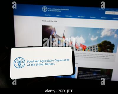 Persona che possiede uno smartphone con il logo dell'agenzia delle Nazioni Unite per l'alimentazione e l'agricoltura (FAO) sullo schermo di fronte al sito web. Concentrarsi sul display del telefono. Foto Stock