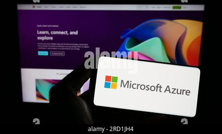 Persona che possiede uno smartphone con il logo della piattaforma di cloud computing Microsoft Azure sullo schermo davanti al sito Web. Concentrarsi sul display del telefono. Foto Stock