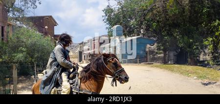 Cowboy o pistolero in cima al cavallo fermarlo guardando indietro alla ricerca del suo nemico su una strada sterrata in una tipica città nella selvaggia e lontana America Foto Stock