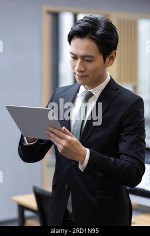 Giovane uomo d'affari cinese che utilizza un tablet digitale in ufficio Foto Stock