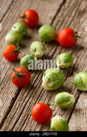 Pomodori ciliegini e cavoletti di Bruxelles su uno sfondo di legno invecchiato. Mix di verdure fresche e sane. Il concetto di alimentazione corretta e sana. Foto Stock