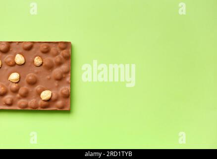 Cioccolato fatto a mano con nocciole intere su sfondo verde brillante, vista dall'alto, spazio copia. Foto Stock