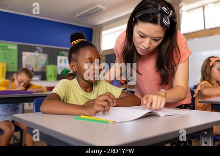 Insegnante femminile felice e diversificata con le studentesse che insegnano a scuola a scrivere in classe Foto Stock