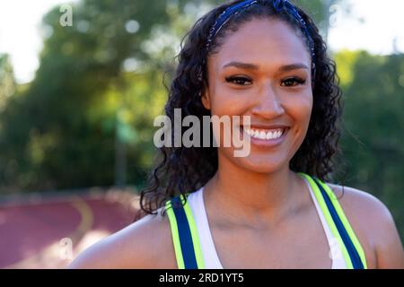 Ritratto di una giocatrice di basket birazziale felice che indossa una maglietta blu bianca sul campo da basket Foto Stock