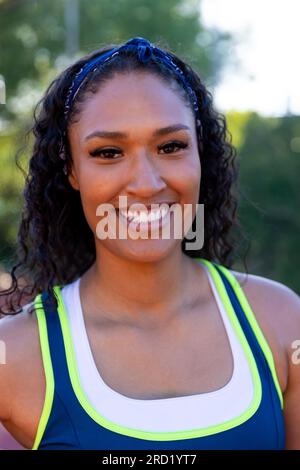 Ritratto di una giocatrice di basket birazziale felice che indossa una maglietta blu bianca sul campo da basket Foto Stock