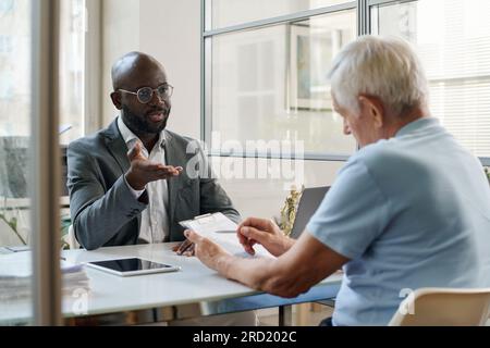 Uomo anziano che legge le condizioni del contratto mentre ha un incontro con l'avvocato in carica Foto Stock