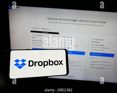 Persona che possiede uno smartphone con il logo della società statunitense di hosting di file Dropbox Inc. Sullo schermo di fronte al sito Web. Concentrarsi sul display del telefono. Foto Stock