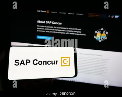 Persona che possiede uno smartphone con il logo del software di gestione delle spese SAP concorda sullo schermo davanti al sito Web. Concentrarsi sul display del telefono. Foto Stock