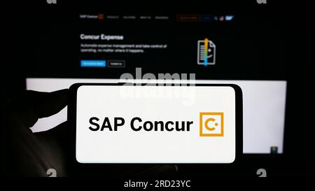 Persona che possiede il cellulare con il logo del software di gestione delle spese SAP concorda sullo schermo davanti alla pagina Web aziendale. Concentrarsi sul display del telefono. Foto Stock