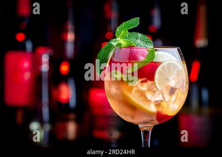 Sangria rosa bevanda alcolica estiva con vino rosa, pesca, arancia, lime e ghiaccio. Sfondo nero bar, utensili da bar in acciaio e bottiglie Foto Stock