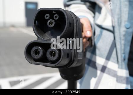 Donna con connettore femmina CCS tipo 2. Spina del connettore combinato 2 del sistema di ricarica combinata rapida per veicoli elettrici presso la stazione EV. Collegamento del caricabatterie per auto. Foto Stock