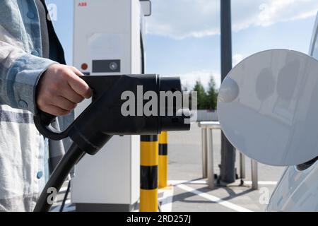 Donna con connettore femmina CCS tipo 2. Spina del connettore combinato 2 del sistema di ricarica combinata rapida per veicoli elettrici presso la stazione EV. Collegamento del caricabatterie per auto. Foto Stock