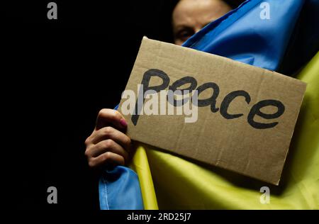 Donna con bandiera Ucraina e cartello di pace. Protesta contro l'invasione della Russia e la guerra contro l'Ucraina. Attacco russo, dimostrazione contro la guerra. Foto Stock