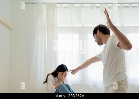 Violenza domestica, marito asiatico minacciando moglie, madre spaventata abbracciare è lei mentre si siede insieme a letto. Foto Stock