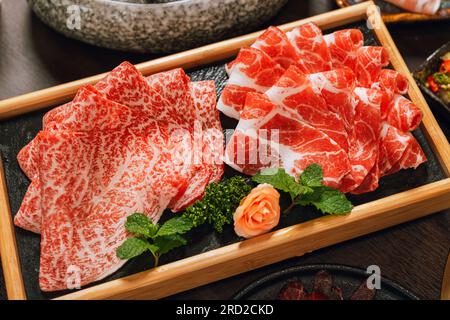 Rare fette di maiale pregiate con consistenza marmorizzata su un piatto di legno circolare servito per pentole calde e Shabu. Foto Stock