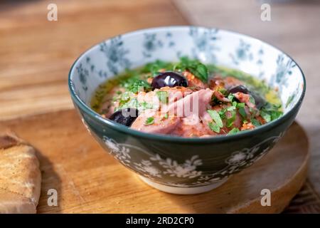 Una singola porzione di Tapas di hummus di barbabietola servita in una ciotola con Olive nere e un condimento alle erbe in un bar di tapas. Foto Stock