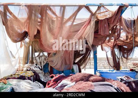 Un assortimento di reti da pesca da traino appese ad asciugare sul lato di un piccolo porto di pesca. Le reti essiccate sono impilate sotto di esse Foto Stock