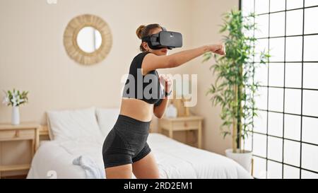 Giovane bella donna ispanica che usa occhiali per realtà virtuale in camera da letto Foto Stock