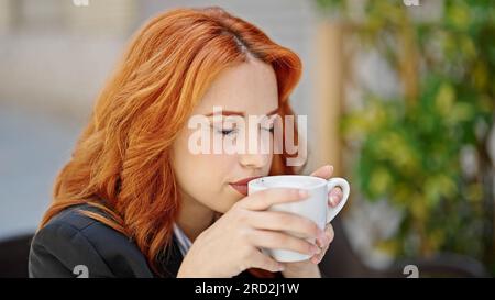 Una giovane donna rossa lavoratrice d'affari che puzza di caffè sulla terrazza della caffetteria Foto Stock