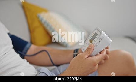Giovane uomo ispanico che misura l'impulso usando il tensiometro a casa Foto Stock