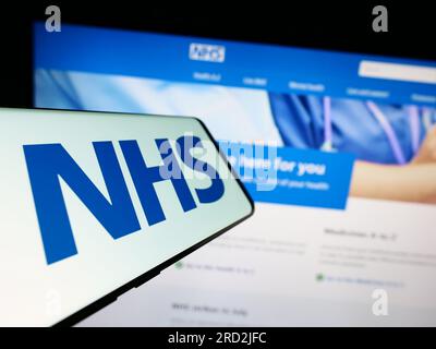 Cellulare con logo del servizio sanitario Nazionale britannico (NHS) sullo schermo davanti al sito web. Concentrarsi sul centro del display del telefono. Foto Stock