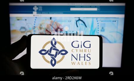 Persona che detiene lo smartphone con il logo del sistema sanitario britannico NHS Galles sullo schermo di fronte al sito Web. Concentrarsi sul display del telefono. Foto Stock