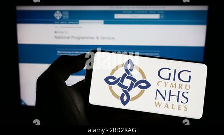 Persona che tiene il cellulare con il logo del sistema sanitario britannico NHS Galles sullo schermo di fronte alla pagina web. Concentrarsi sul display del telefono. Foto Stock
