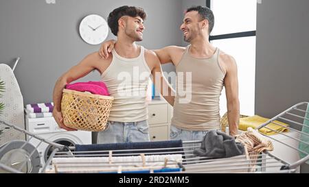 Due uomini si abbracciano tenendo un cestino di vimini con i vestiti nella lavanderia Foto Stock
